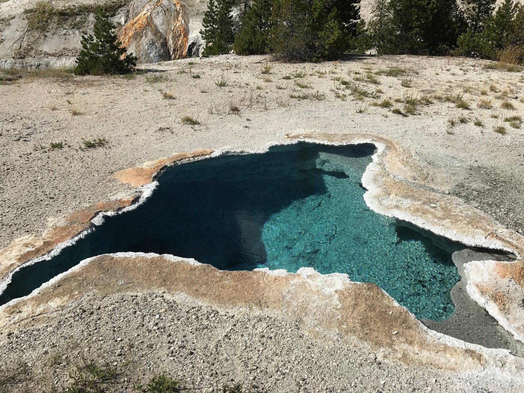 Clear deep blue geothermal spring edged by pale mineral deposits