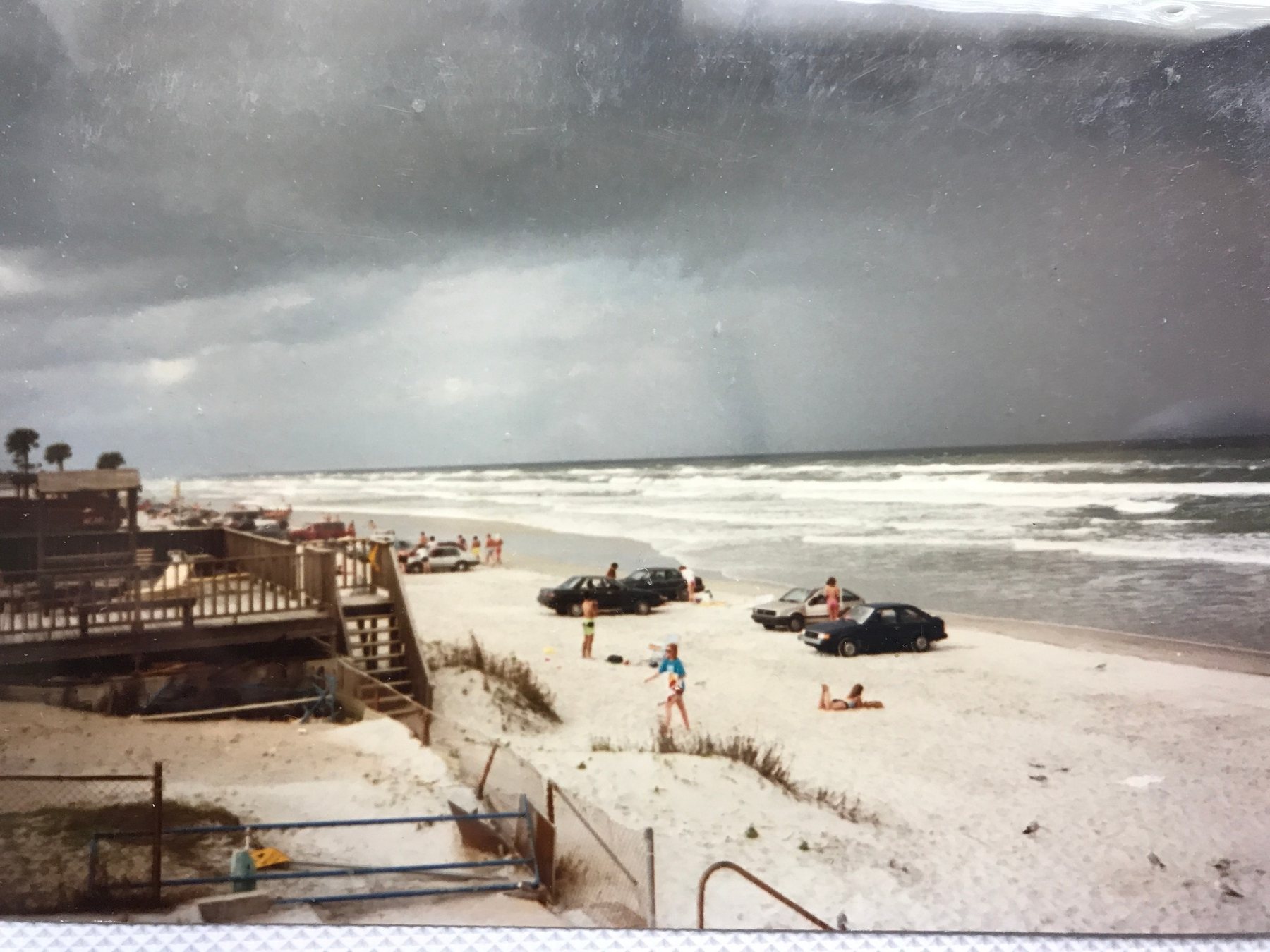 People and parked cars on a beach beneath an approaching storm