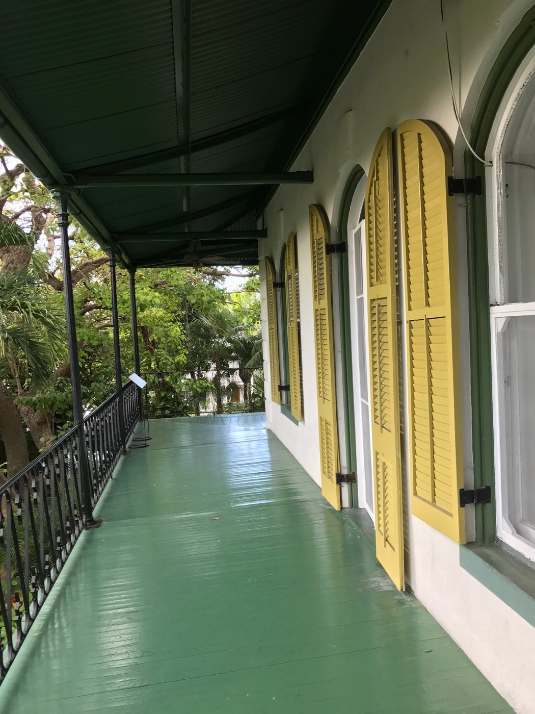 Historic veranda with green floor, dark awning, and yellow shutters
